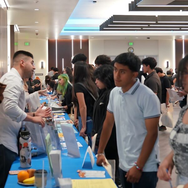 Students and young adults engage with organization representatives across multiple booths during a job and resource fair in a modern, well-lit event space.
