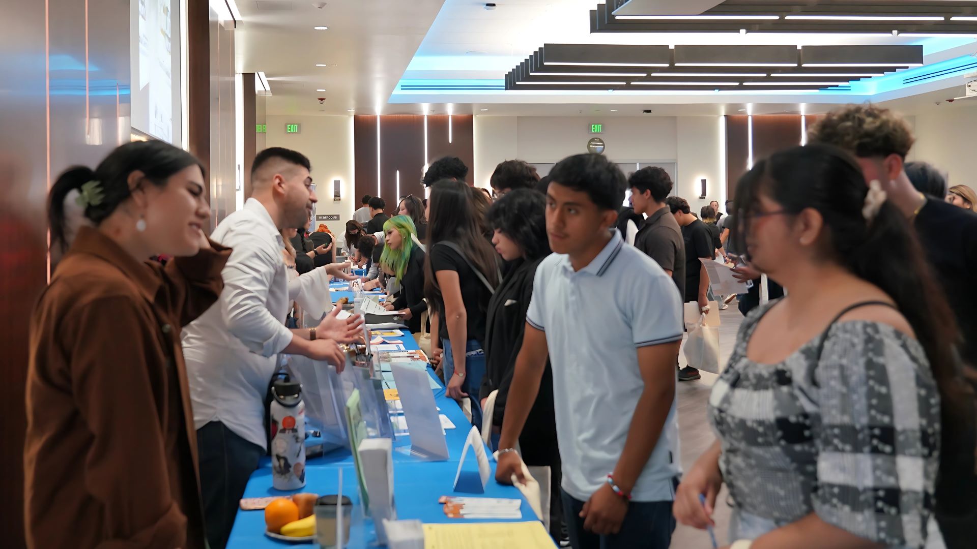 Students and young adults engage with organization representatives across multiple booths during a job and resource fair in a modern, well-lit event space.