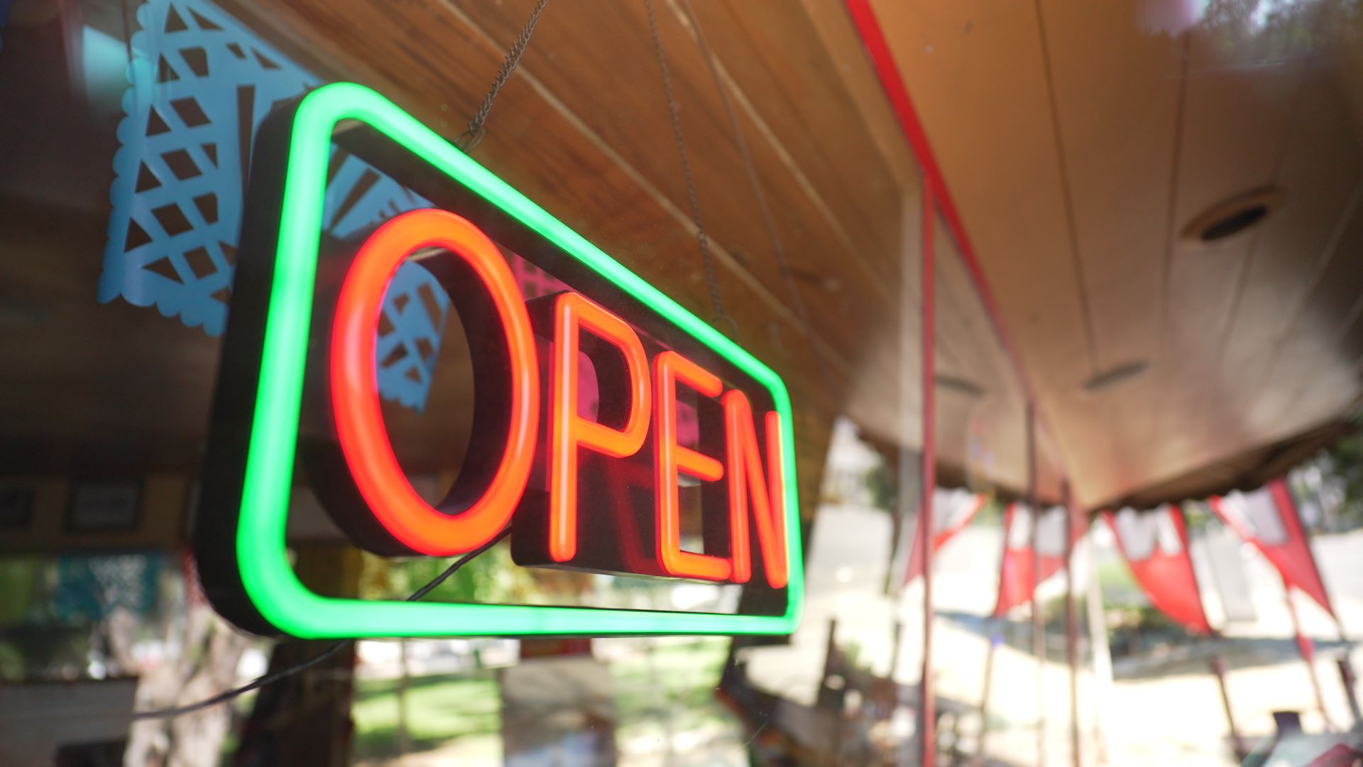 A brightly lit neon “OPEN” sign with red letters and a green border hangs in a shop window, signaling that the business is open.