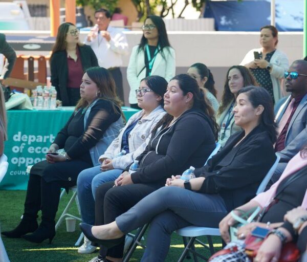 A seated audience listens attentively during an outdoor event hosted by the Department of Economic Opportunity.