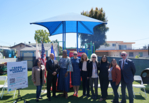 Ten individuals stand together in front of a playground at an outdoor event for the Department of Economic Opportunity’s “Earn While You Learn” program.