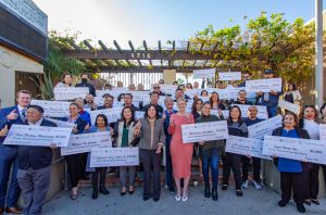 ChatGPT said: Grant recipients pose with large checks and thumbs up in celebration of receiving funding through the Department of Economic Opportunity.