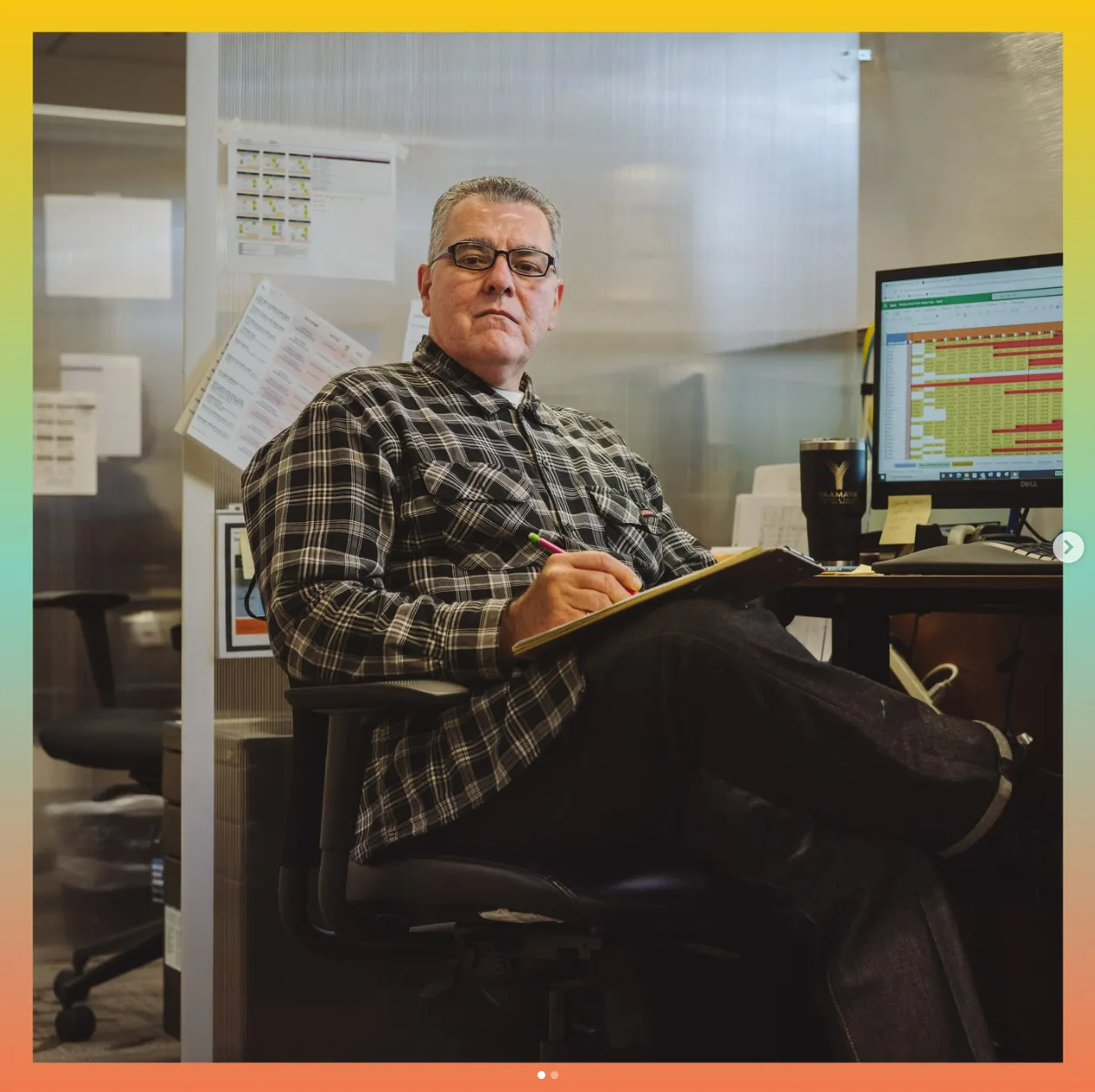 Man with a ledger and pen, sitting in a chair in an office.